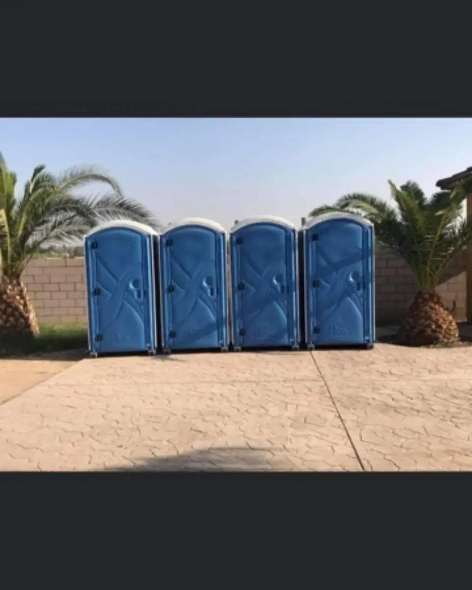 Four blue portable toilets lined up outdoors for an event